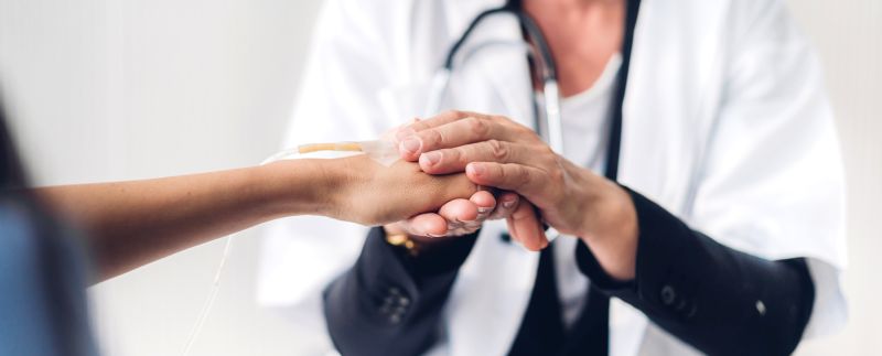 Lekarz trzyma rękę pacjenta z kroplówką, wyrażając wsparcie i empatię w klinicznym otoczeniu.
